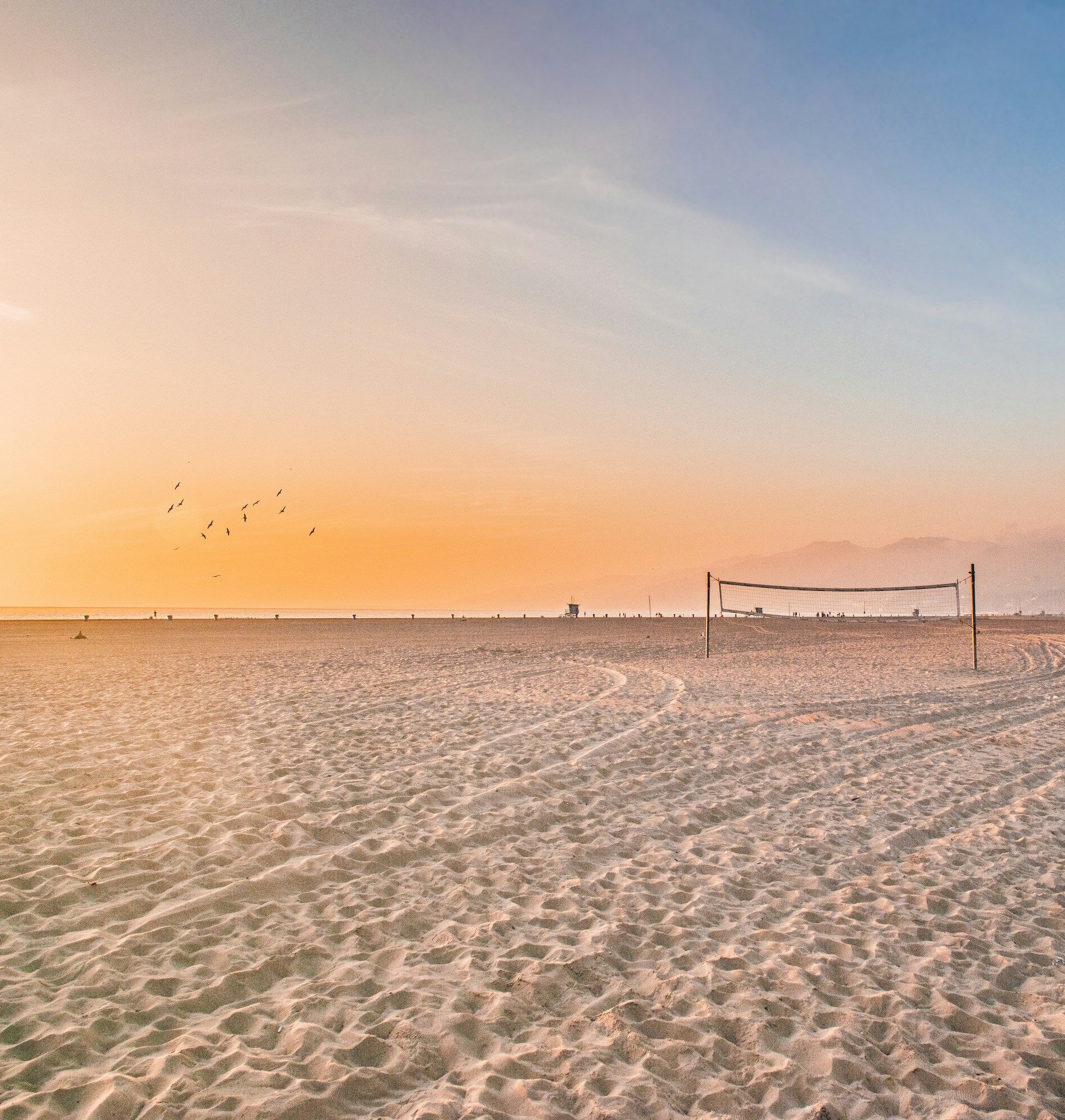 A beach volley court on the sand by the sea at sunset.